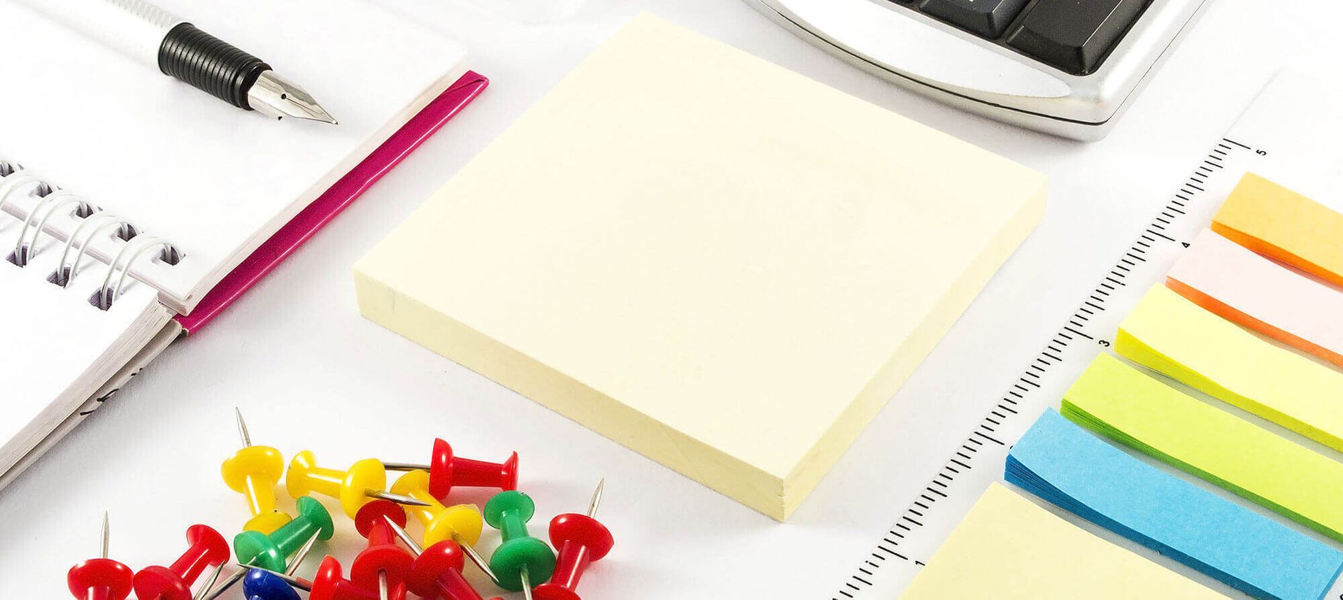 Bunte Klebezettel, Reißzwecken, Notizbuch und Stift auf weißem Hintergrund.